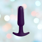 A black VeDO Bump Waterproof Anal Vibrator with an ergonomic design and a T-shaped base is centered against a soft-focus background featuring pastel-colored bokeh lights.